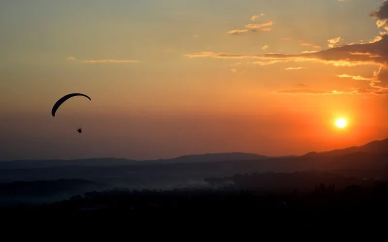 Paraglider silhouette gliding across a vibrant orange sunset sky over Bir Billing