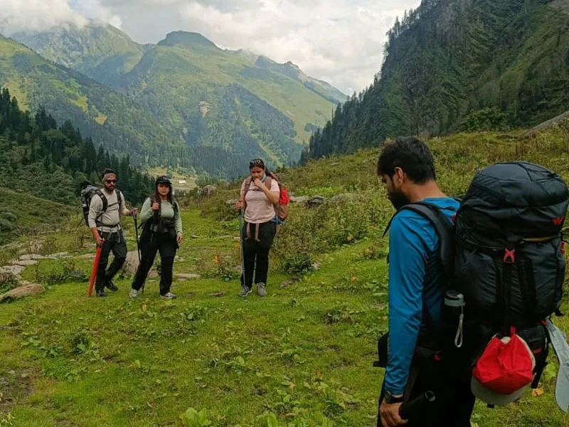 Hikers with heavy backpacks trekking through alpine meadows near Manali