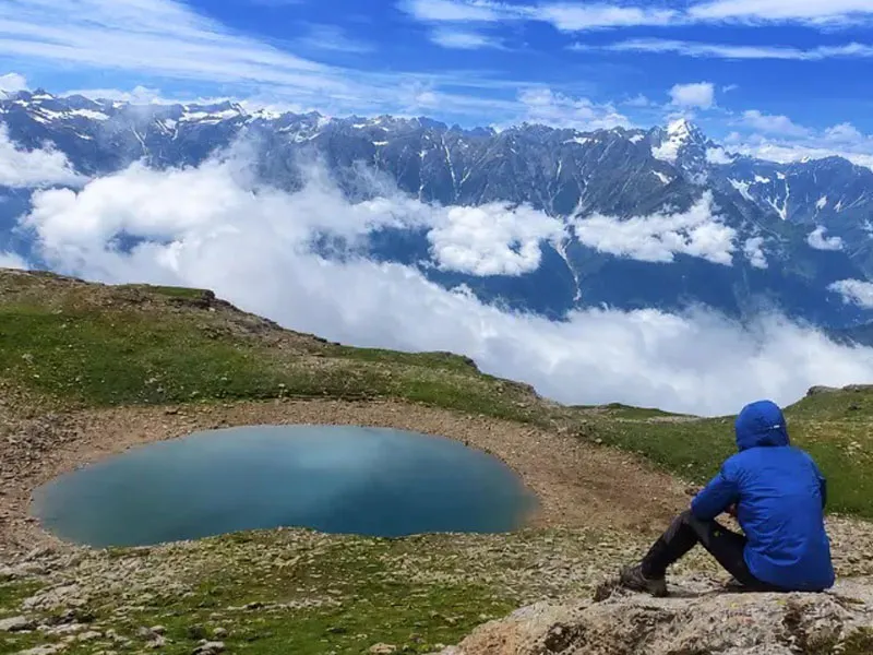 Hiker sitting on a ridge overlooking the sacred turquoise waters of Bhrigu Lake