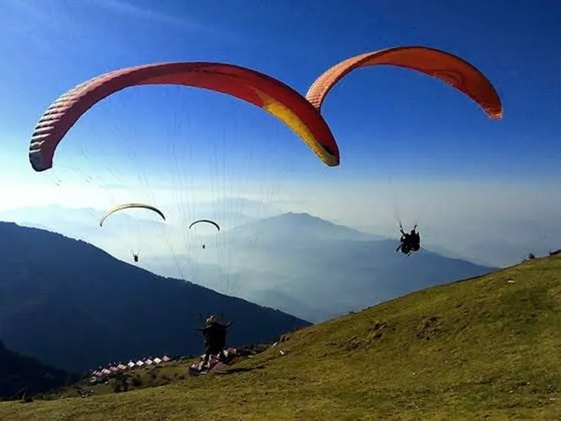 Tandem paraglider soaring across a clear blue sky over high mountain slopes in Bir Billing