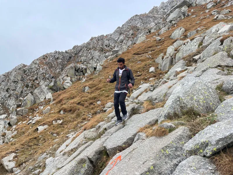 Trekker descending steep granite boulder trail with red trail markers on Indrahar Pass trek