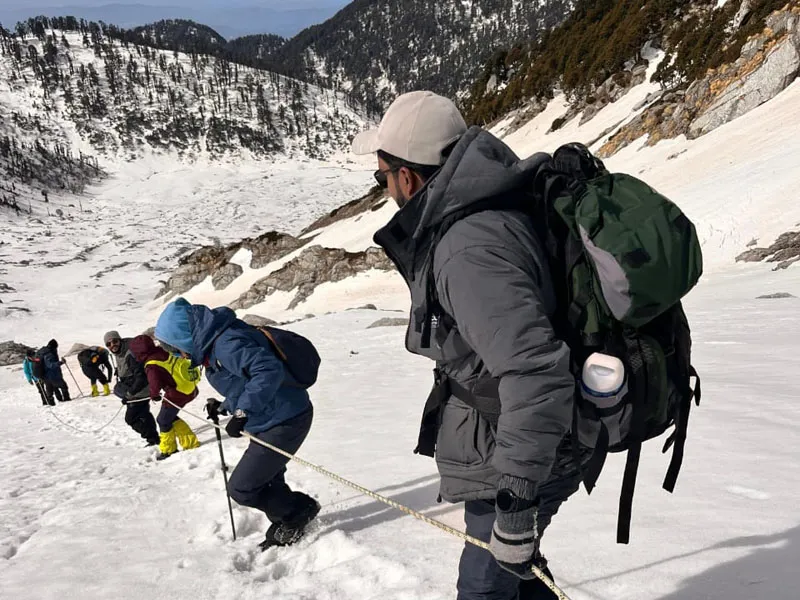 Trekkers ascending a steep snowy mountain slope using fixed safety rope on Indrahar Pass