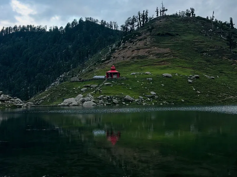 Serene reflection of surrounding green hills and temple in the clear waters of Kareri Lake
