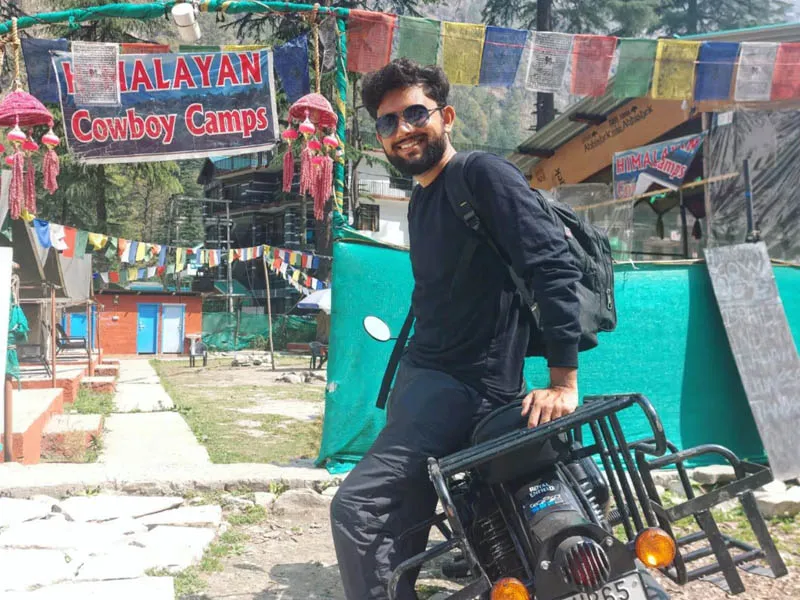 Biker posing with touring motorcycle outside a riverside campsite in Kasol