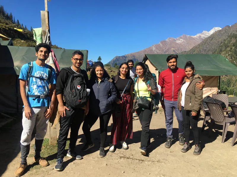 Trekking group standing together at Kheerganga alpine campsite with mountain views