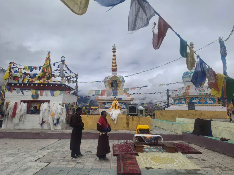 Tibetan Buddhist monks standing near ancient white stupas and prayer flags in Spiti Valley