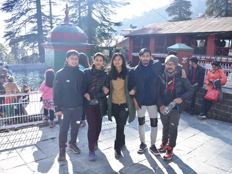 Group of young travelers posing outdoors at an ancient stone temple courtyard in McLeodganj