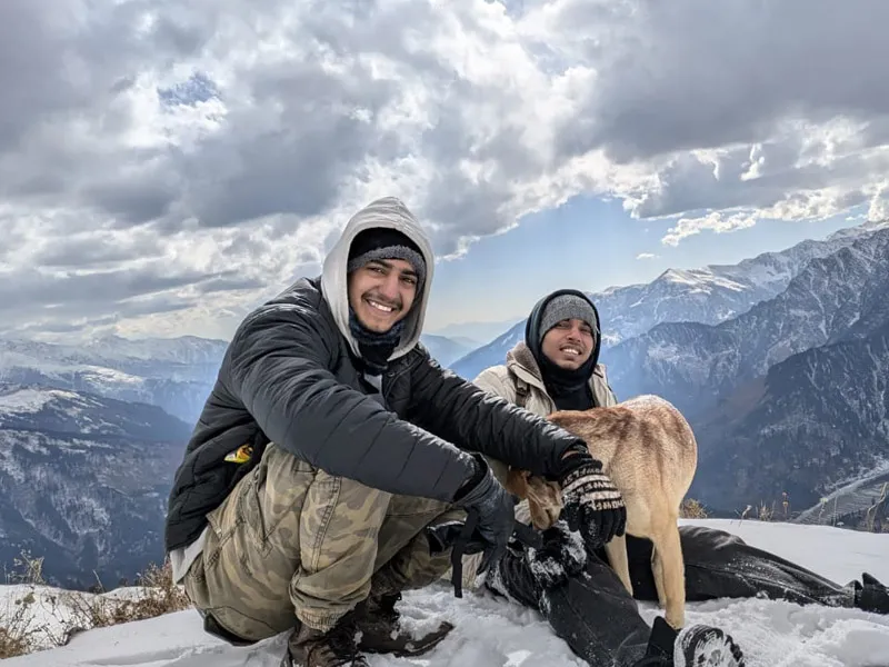 Trekkers smiling with a mountain dog on a deep snow slope overlooking Himalayan ranges