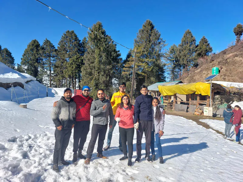 Group of travelers posing on a snow-dusted trail outside village cottages on Prashar Lake trek