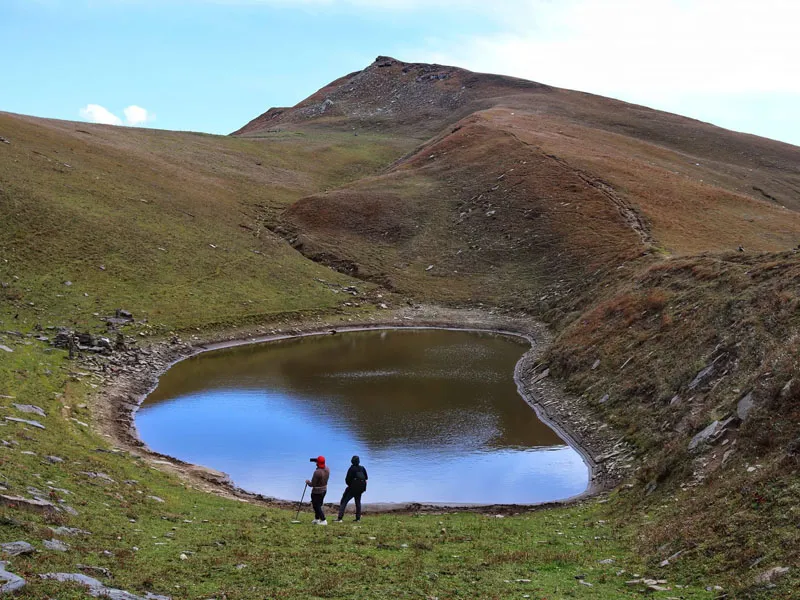 Two trekkers standing by the shores of pristine circular Ranisui Lake nestled in alpine meadows