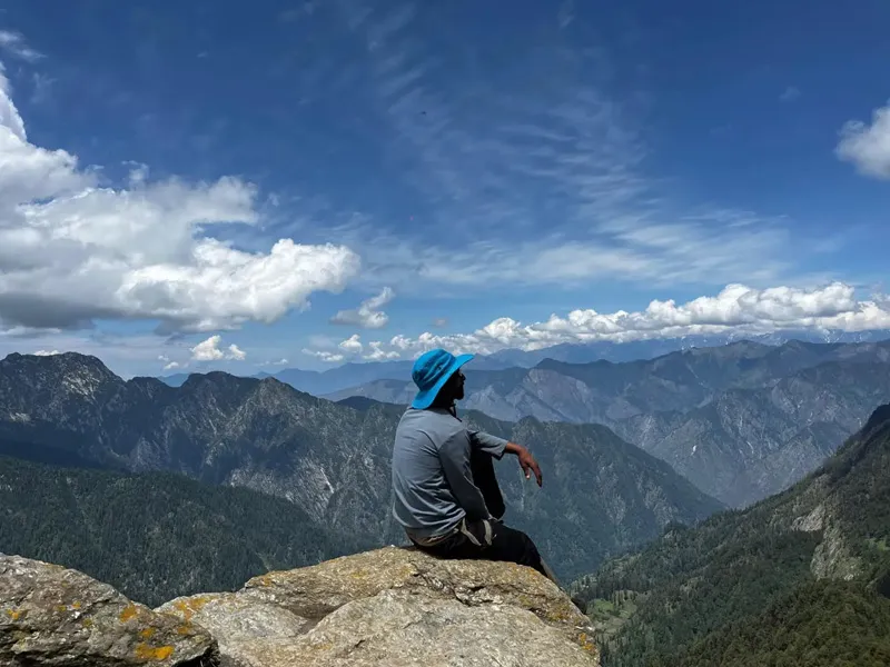 Hiker sitting on a rock edge enjoying panoramic vistas of distant mountain ranges