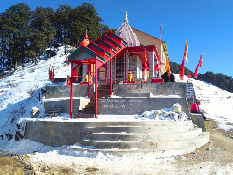 Ancient stone shrine of Mahakali Temple adorned with red flags covered in winter snow