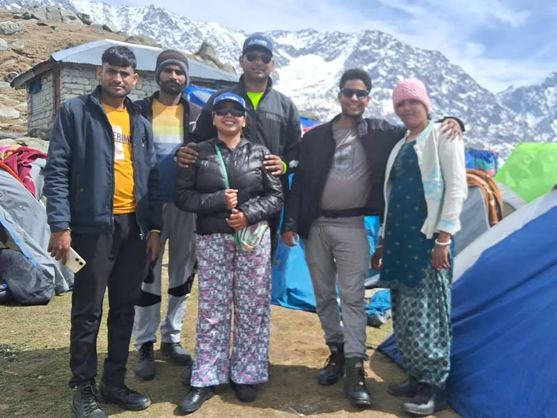 Trekking team smiling together outside campsite tents with Dhauladhar ranges in the background