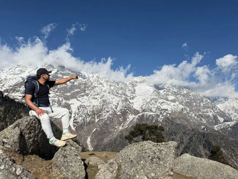 Hiker sitting on a granite rock with dramatic snow-covered Dhauladhar mountain peaks in the background on Triund trek