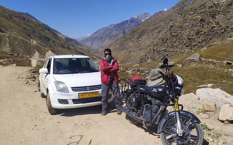 Touring motorcycle and white car parked along an arid mountain pass road in Spiti Valley